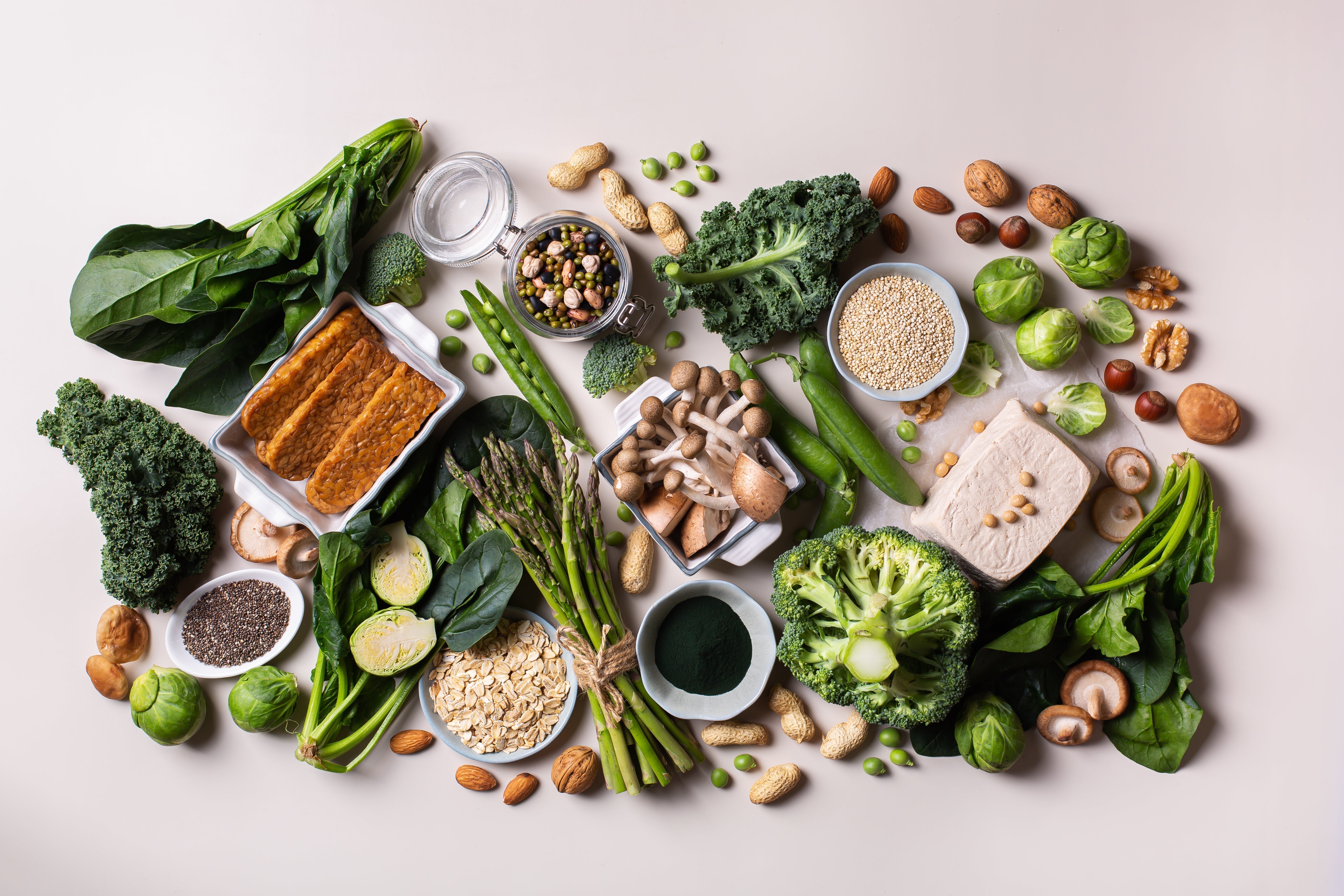 Vue de dessus d'une sélection d'aliments riches en protéines végétales : tofu, tempeh, quinoa, flocons d'avoine, spiruline, brocoli, épinards, chou kale, champignons, graines de chia, noix, amandes et légumineuses.