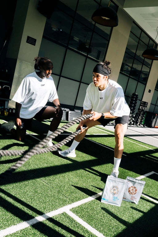 Deux athlètes QNT s'entraînent aux battle ropes en salle de sport avec des sachets de Light Digest Whey Protein — protéine légère idéale pour l'entraînement fonctionnel
