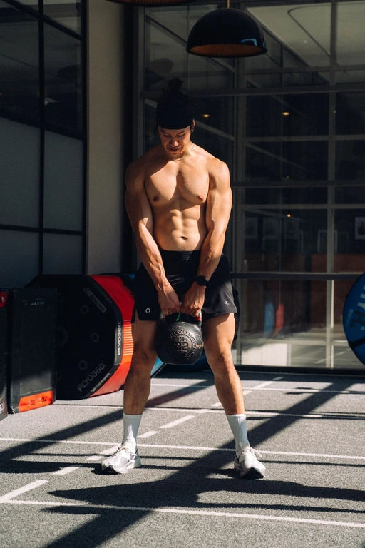 Athlète musclé réalisant un exercice de kettlebell en salle de sport — entraînement de force et musculation avec QNT Sport